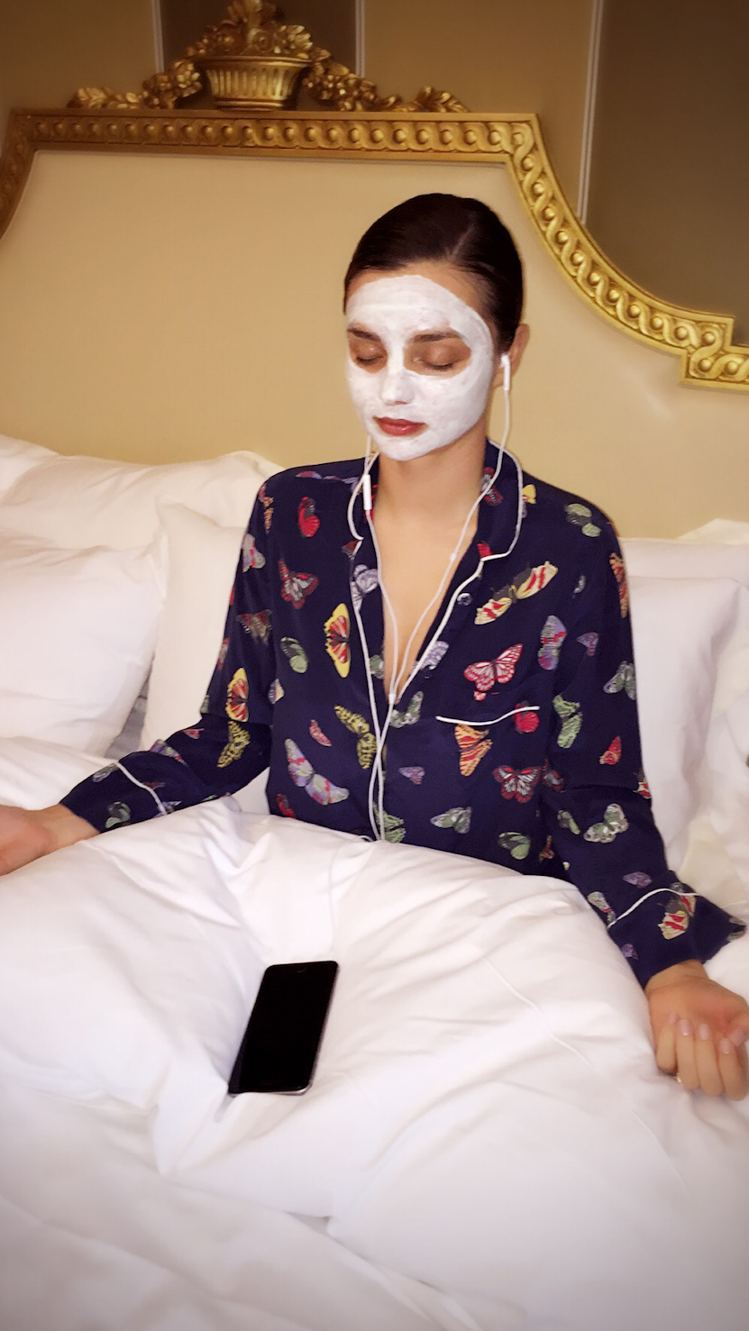 Miranda Kerr listening to a meditation in bed with a face mask on