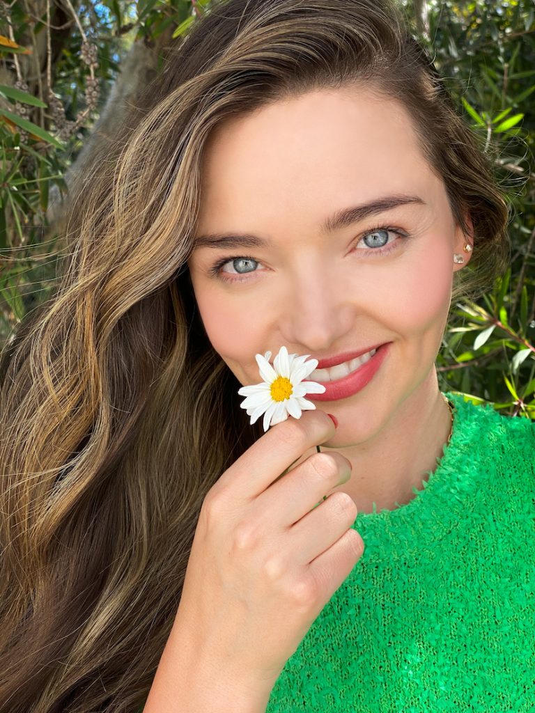 Miranda in green jumper holding a daisy for world kindness day