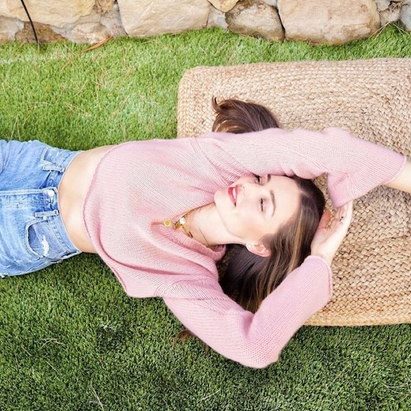 Miranda Kerr lying on grass in pink jumper and blue jeans