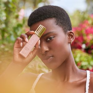 Woman holding serum over eye in field of flowers